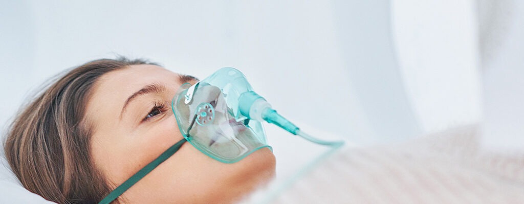 Oseba leži in diha kisik skozi masko v hiperbarični komori