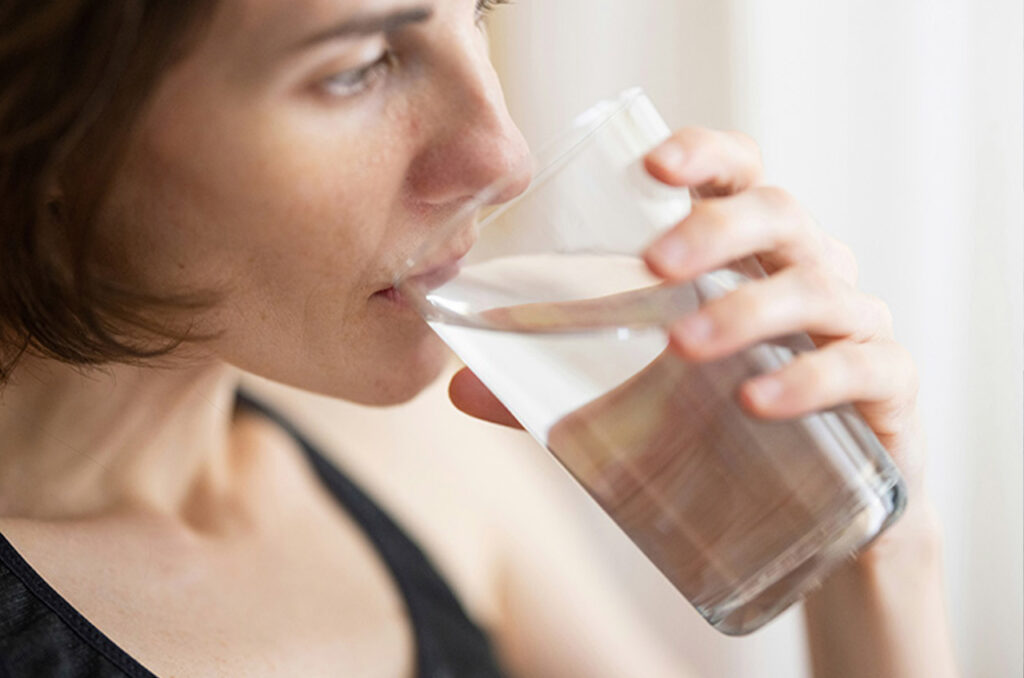 Oseba pije kozarec vode ob naravni svetlobi